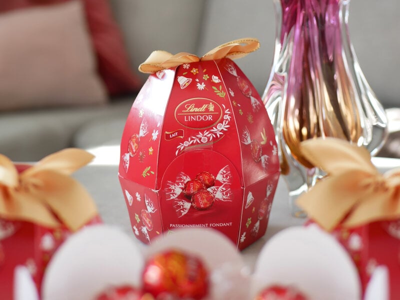 Äggformad förpackning i papp, fylld med ljuvliga Lindt chokladkulor. Röd botten, text och bilder i rött/vitt/guld.