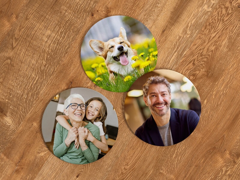 Finn den ultimata personliga gåvan hos Coolstuff! Runda coasters/glasunderlägg försedda med personliga foton. Här, exempel på ett underlägg med en hund i ett maskrosfält, ett underlägg med en kvinna i grön tröja med ett barn som slingrar sig runt halsen och så ett underlägg med en glad skäggig man i grån T-shirt och blå kofta. Underläggen ligger på ett underlag av trä.